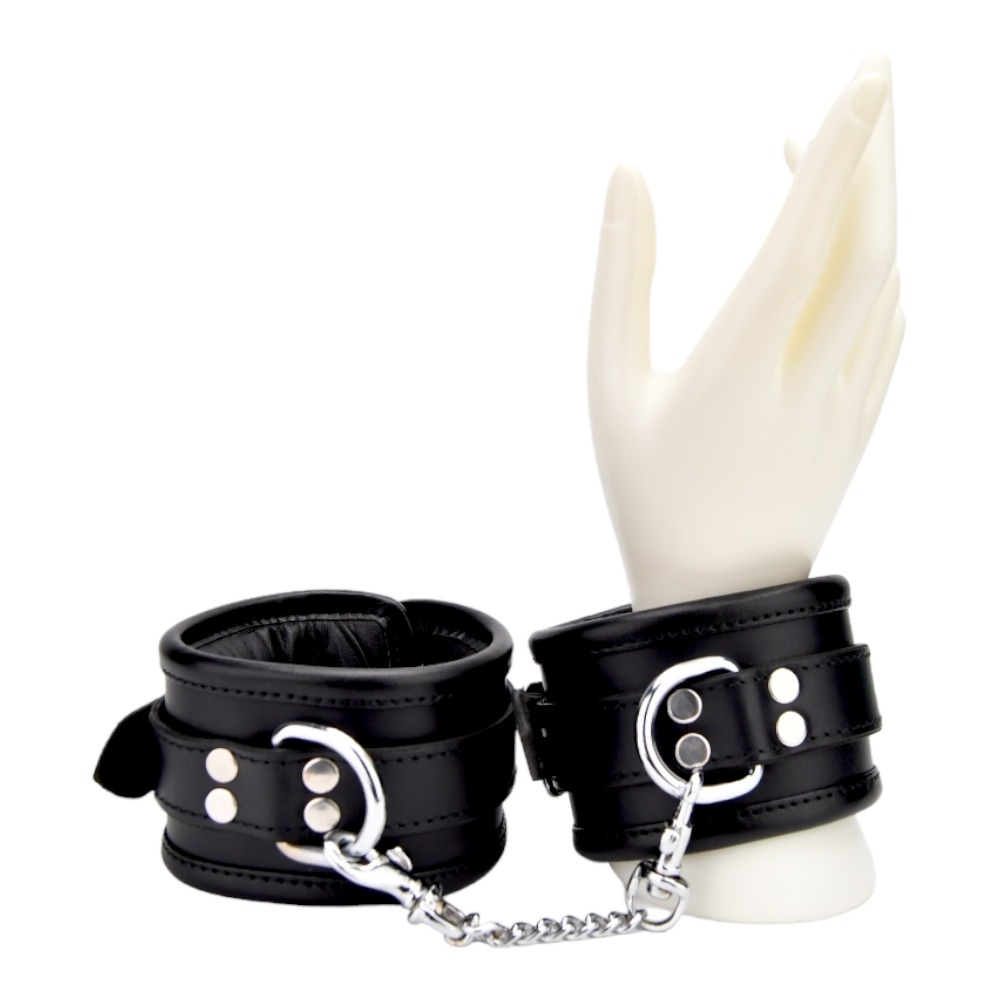 Bound Leather Wrist Restraints, Padded black leather wrist cuffs with silver trims joined by a short metal chain